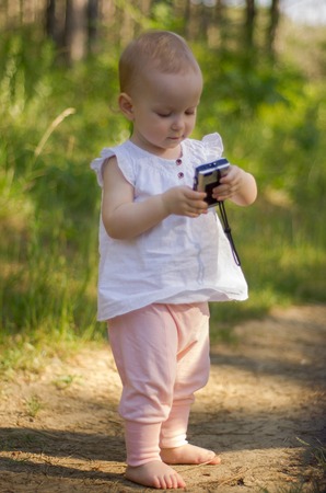Sweet little girl, on a forest path, holds a camera in her hands. Outdoor.の写真素材