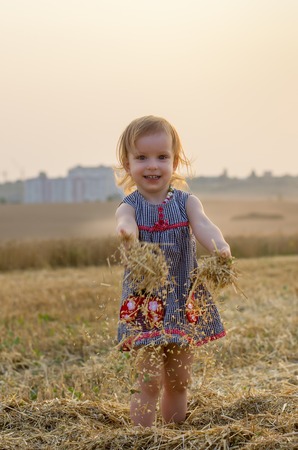 Happy family: Little girl playing with straw, on a wheat field. the orange field on a sunny summer day. Parents and kids relationship. Nature in the country.の写真素材
