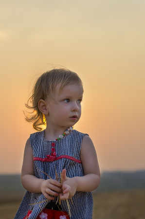 Happy family: Little girl playing with straw, on a wheat field. the orange field on a sunny summer day. Parents and kids relationship. Nature in the country.の写真素材