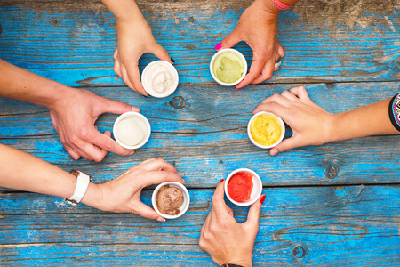 Female and male hands take the ice cream. The choice of refined flavors of Italian ice cream in bright colors is served in individual porcelain cups on an old rustic wooden table in ice cream, a top view with a copy of the space.の写真素材