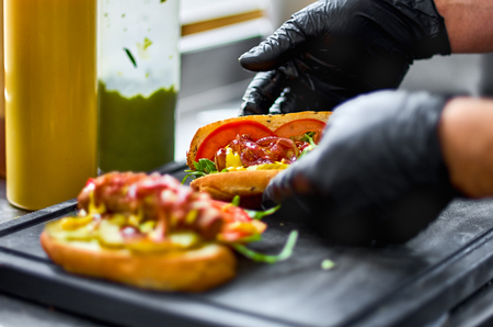 The cook prepares a hot dog, adding the sauce to the sausage. Two hamburgers, hot dog. concept of fast foodの写真素材