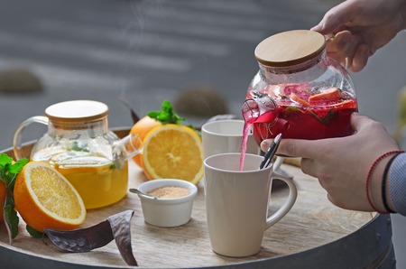 Hands of a man pour orange tea with ginger and raspberries on a wooden backgroundの写真素材