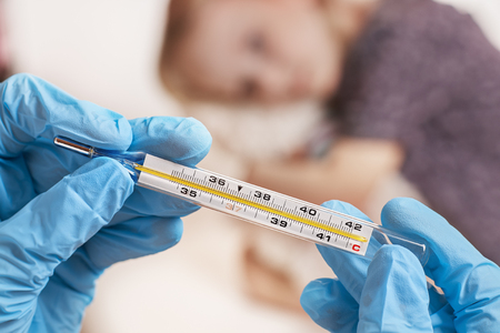 Close Up shot at a thermometer. Hands in medical gloves hold a mercury thermometer. A little girl is measured by temperature. Shallow depth of field with a focus on the thermometer. selective focus.の写真素材