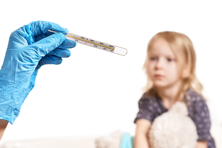 Close Up shot at a thermometer. Hands in medical gloves hold a mercury thermometer. A little girl is measured by temperature. Shallow depth of field with a focus on the thermometer. selective focus.の写真素材