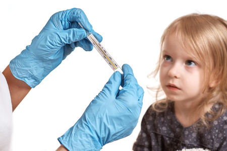 Close Up shot at a thermometer. Hands in medical gloves hold a mercury thermometer. A little girl is measured by temperature. Shallow depth of field with a focus on the thermometer. selective focus.の写真素材
