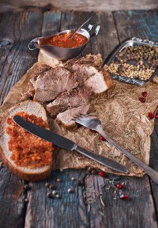 Baked succulent pork meat, sliced pieces on parchment paper, close-up with bread and tomato sauce, dark wooden rustic background. Concept of healthy food.の写真素材