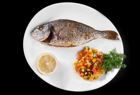 fish grill dish baked whole grilled on a plate with vegetables and lemon on top for the menu on a...