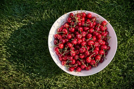 Red ripe cherries on a white plate on green grass. summer berries, natural vitamins, healthy food