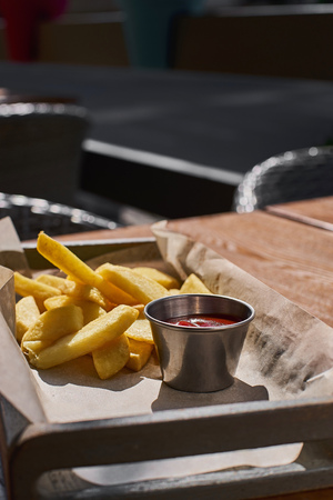 French fries and ketchup in a basket, on a terrace under bright sunlight