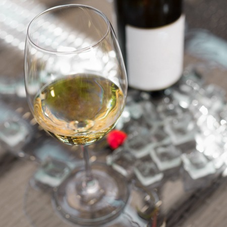 White wine in a glass with ice, old wooden background, selective focus, square frame 1:1