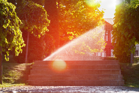 beautiful landscape with automatic sprinkler spraying watering the lawn in the home garden with a with sunbeam in water drops close up. gardening conceptの写真素材
