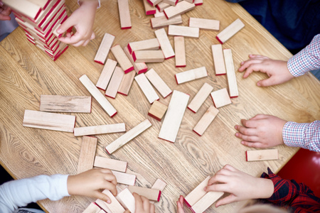 The child plays in a tower of wooden bars. Floors of wooden pieces. The child takes out the bars from the floors of the tower. Board game.の写真素材