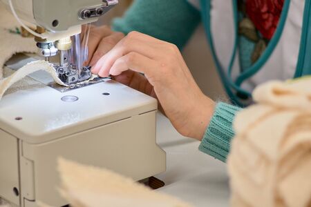 Chisinau, Moldova, March 12, 2019. A young woman who works as a seamstress in purple uniform sews baby clothes on a sewing machine on a table in a sewing workshop. Job creation.のeditorial素材