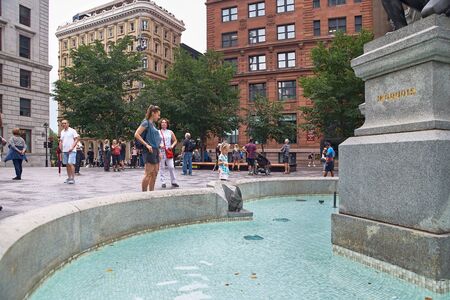Montreal, Quebec, Canada September 3, 2018: Journey, a little girl throwing a coin into the fountain of Paul Chomedey de Maisonneuve, at Place d'Armes in Montreal, for good luck. Happy young parents and little children traveling together on a travel vacatのeditorial素材