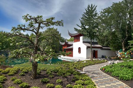 MONTREAL, CANADA, September 5, 2018: Beautiful small pine tree growing in yellow flowerbed with pond and pretty pavilion in Montreal s Botanical Gardens, Montreal, Quebecのeditorial素材