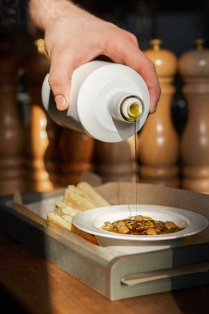Traditional Mediterranean snack. Cook pours olive oil on a Hummus with pine nuts, olive oil, served on a plate with pita bread, served in a restaurant. Sunlight illuminated from the window, low keyの写真素材