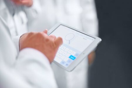 Employees confer stand in white coats using a tablet computer and telephone. close up of hand with...