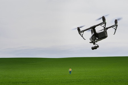 Man goes to the field. Man from behind, a quadrocopter is flying behind him. Green field in the...