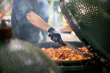 Hand of young man grilling some meat grill. Shallow DOF . Street market, street trading, healthy food. Selective focus.の写真素材