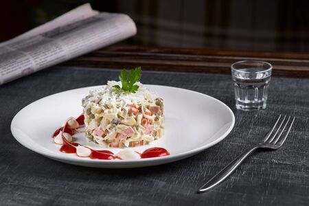 Russian traditional salad Olivier with vegetables and meat. restaurant dish, New Year's salad on a white plate and a glass of vodka. Close-up. Gray backgroundの写真素材