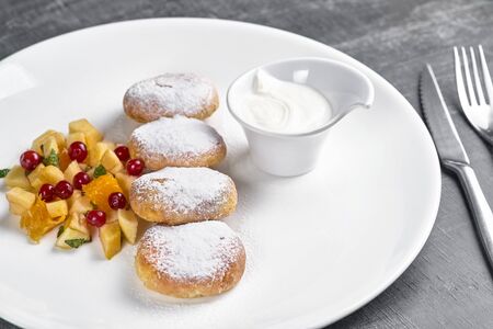 Healthy breakfast Russian cheese curd pancakes with fruit and sour cream for breakfast on a dark wooden background. Free copy space for text. Close up cheese pancake dessert. Selective focus.の写真素材