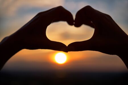 Concept or conceptual woman hands in love, symbol of heart over sky background. Heart shape making of hands against bright sunset and sunny golden.の写真素材