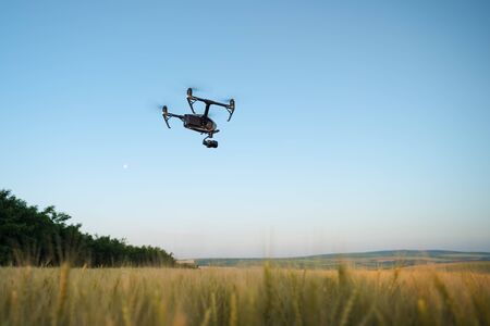 Quadcopter with camera flying over field. Photography quadcopter drone hovering over young green...