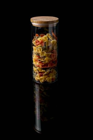 Raw spaghetti in the shape of a butterfly in the glass pot isolated on black background. Raw fusilli in a jar.の写真素材