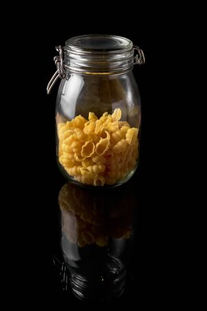 Raw Spaghetti shells in the glass pot isolated on black background. Raw fusilli in a jar.の写真素材