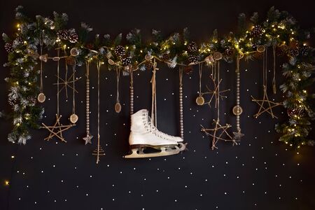 Christmas decorations on a dark wall, Happy Holiday. The wall is decorated with a garland with ate tree branches and white skates. Expectations of winter.の写真素材