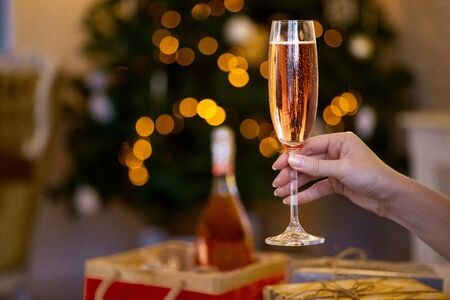 Female hand holding glass of champagne, party celebration. Holidays, people and celebration concept. Christmas tree in the background.の写真素材