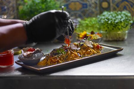 Food concept. The chef garnishes with red caviar a seafood spaghetti dish. Selective focus. Shallow...