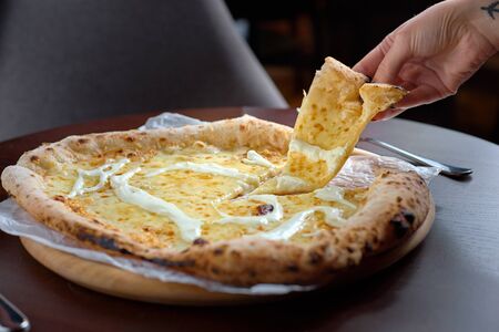 Food concept. Italian Pizza Restaurant Menu - Pizza Quattro formaggi pizza with one slice separated with one slice in a female hand.の写真素材
