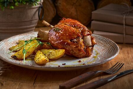 Pork knuckle with baked potatoes on rustic kitchen table at dark wooden background, front view. Pork leg done, German foodの写真素材