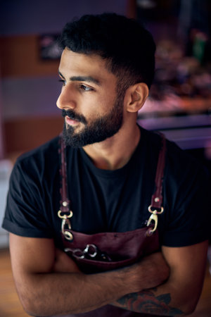 Young hairdresser at his hairdresser. a man with a beard is standing by the window and looking at...