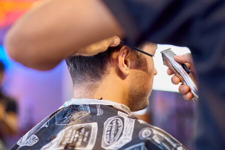 Master cuts hair and beard of men in the barbershop, hairdresser makes hairstyle for a young man....