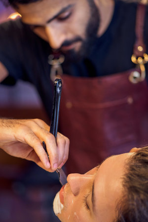 Shaving process of beards in Barbershop. Master makes the client shave his beard with vintage straight razor. Work in the Barber shop, The process of the hairdresser.の写真素材