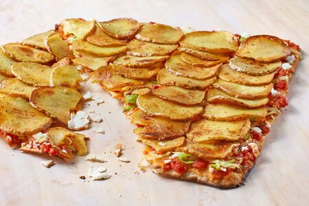 Tarte Flambee or Flammkuchen with potatoes on a wooden cutting board, traditional Alsatian pie,...