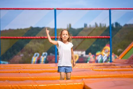 Little pretty girl having fun outdoor. Jumping on trampoline in children zone. Happy girl jumping on the yellow trampoline in Amusement parkの写真素材