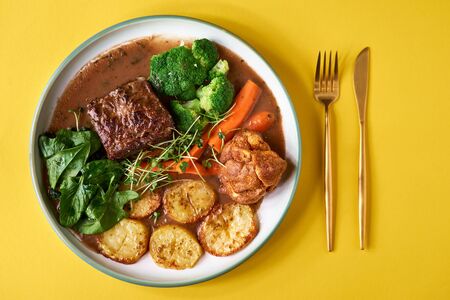 Rare roast beef meal with organic root vegetables and traditional Yorkshire pudding with sauce, stewed vegetables. Shot Top view on yellow background, copy space.の写真素材