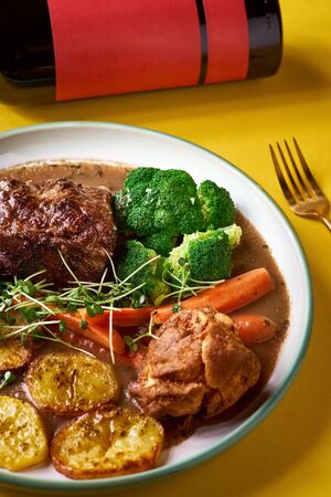 Rare roast beef meal with organic root vegetables and traditional Yorkshire pudding with sauce, stewed vegetables. Shot Top view on yellow background, copy space.の写真素材