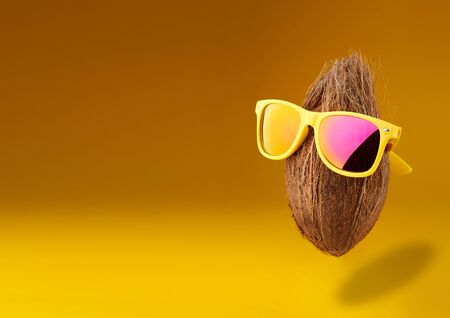 Summer times of funny attractive coconut in stylish sunglasses on a yellow background. minimal fruit concept. Idea creative foods and drinks that are typically enjoyed at summer festivals around the worldの写真素材