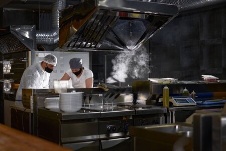 mask on the chefs face in a restaurant: cooks in an open kitchen, a client sees work during a pandemicの写真素材