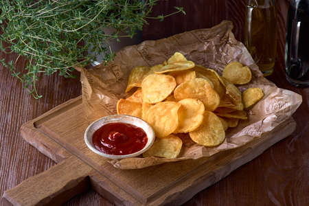 Delicious sweet potato chips with ketchup on a wooden board, beer snack. Concept of unhealthy food.