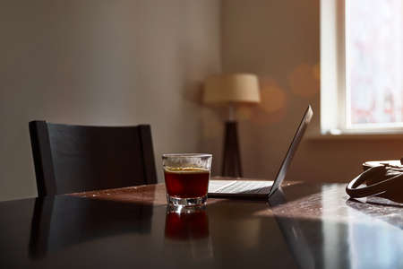 Home work place with laptop, cup of hot drink on table near window on sunset or sunrise. Freelance, working from home, online learning, home office.の写真素材