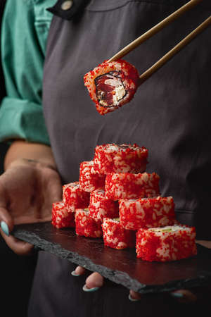 Close-up of a girls hands hold sushi and California rolls on a black stone. Japanese traditional cuisine.の写真素材