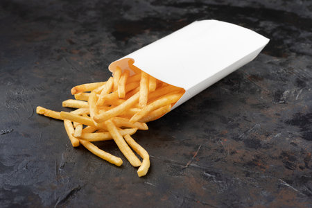 Serving in a paper cone of takeaway potato chips on a rustic on a dark stone surface with copyspace.
