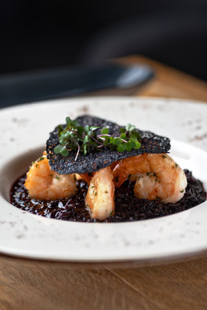 Black rice risotto. Shrimp risotto on a white plate on the table, serving in a restaurant, menu food concept.の写真素材