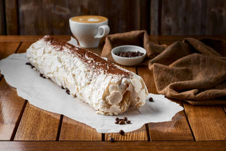 Close-up shot of meringue roll with coffee filling sprinkled with powdered sugar. Copy space,...
