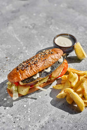 Fried fish sandwich with tartar sauce and french fries on stone background. space for textの写真素材